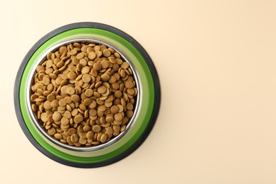 Photo of Dry pet food in feeding bowl on beige background, top view. Space for text