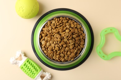 Photo of Dry pet food in feeding bowl and toys on beige background, flat lay