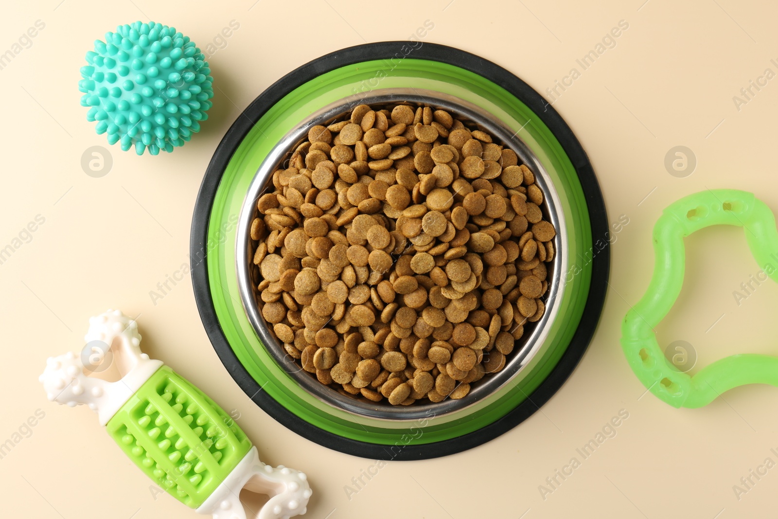 Photo of Dry pet food in feeding bowl and toys on beige background, flat lay