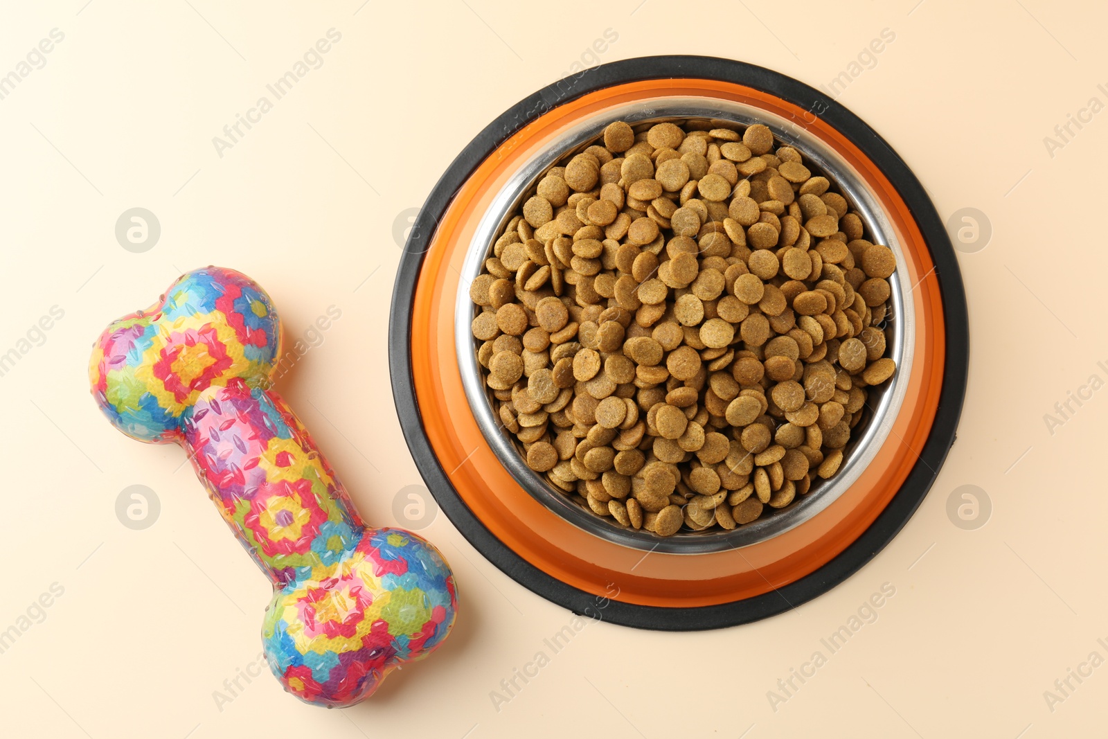 Photo of Dry pet food in feeding bowl and chew bone on beige background, flat lay