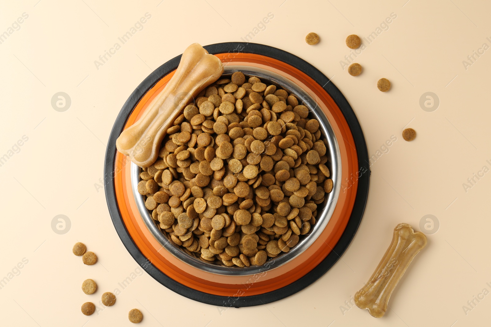 Photo of Dry pet food in feeding bowl and chew bones on beige background, top view