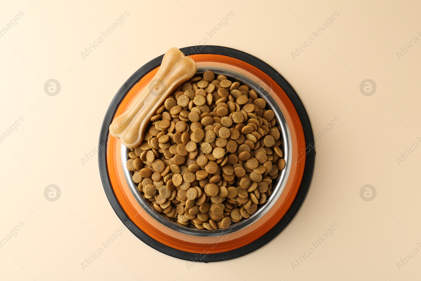 Photo of Dry pet food in feeding bowl and chew bone on beige background, top view