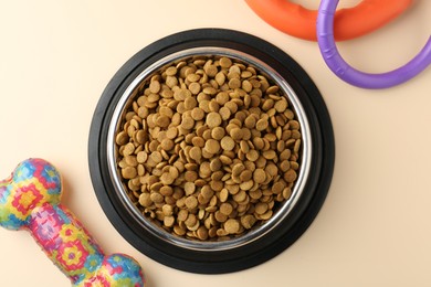 Photo of Dry pet food in feeding bowl and toys on beige background, flat lay