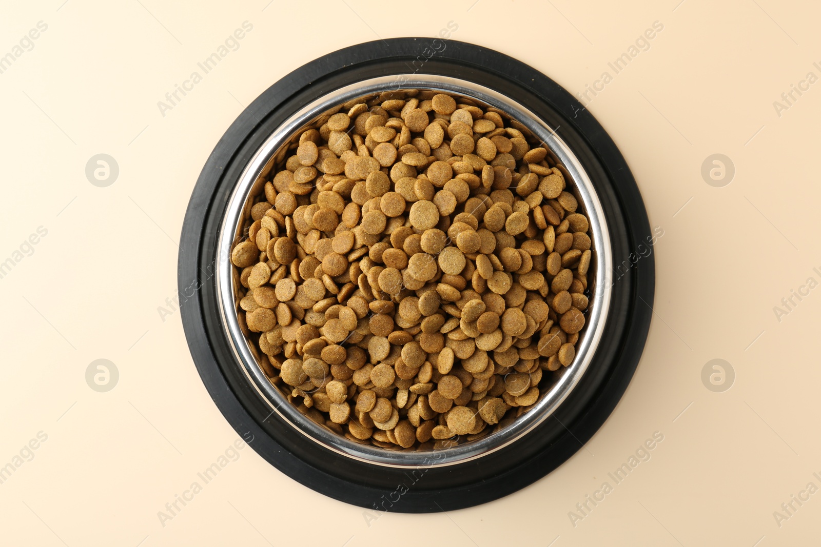 Photo of Dry pet food in feeding bowl on beige background, top view