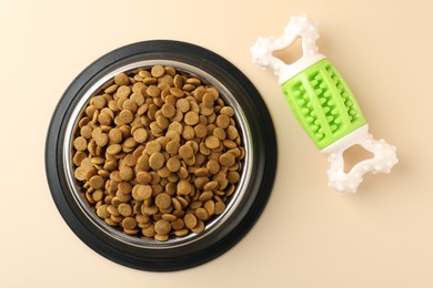 Photo of Dry pet food in feeding bowl and chew bone on beige background, flat lay