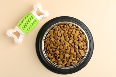 Photo of Dry pet food in feeding bowl and chew bone on beige background, flat lay