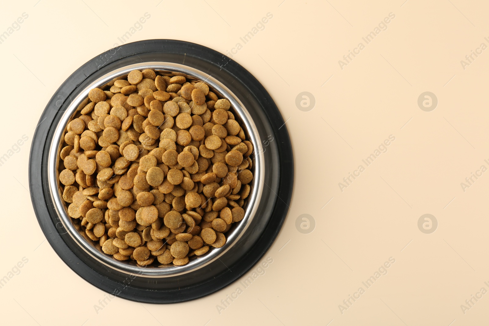 Photo of Dry pet food in feeding bowl on beige background, top view. Space for text