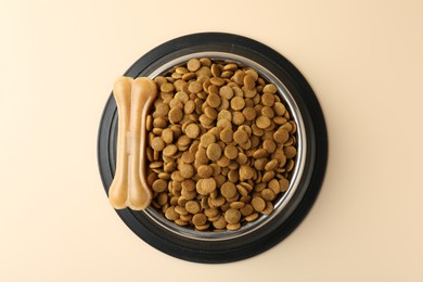 Photo of Dry pet food in feeding bowl and chew bone on beige background, top view