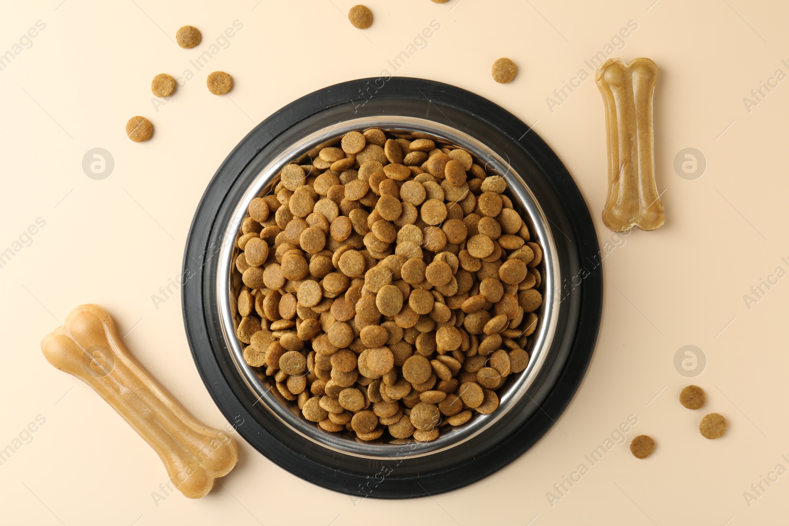 Photo of Dry pet food in feeding bowl and chew bones on beige background, top view