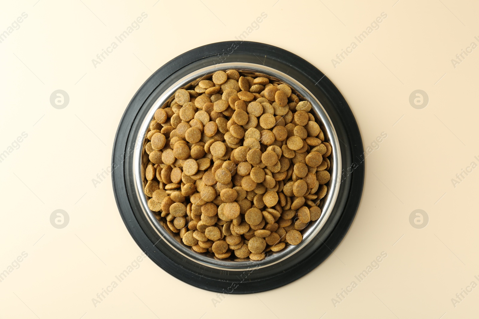 Photo of Dry pet food in feeding bowl on beige background, top view