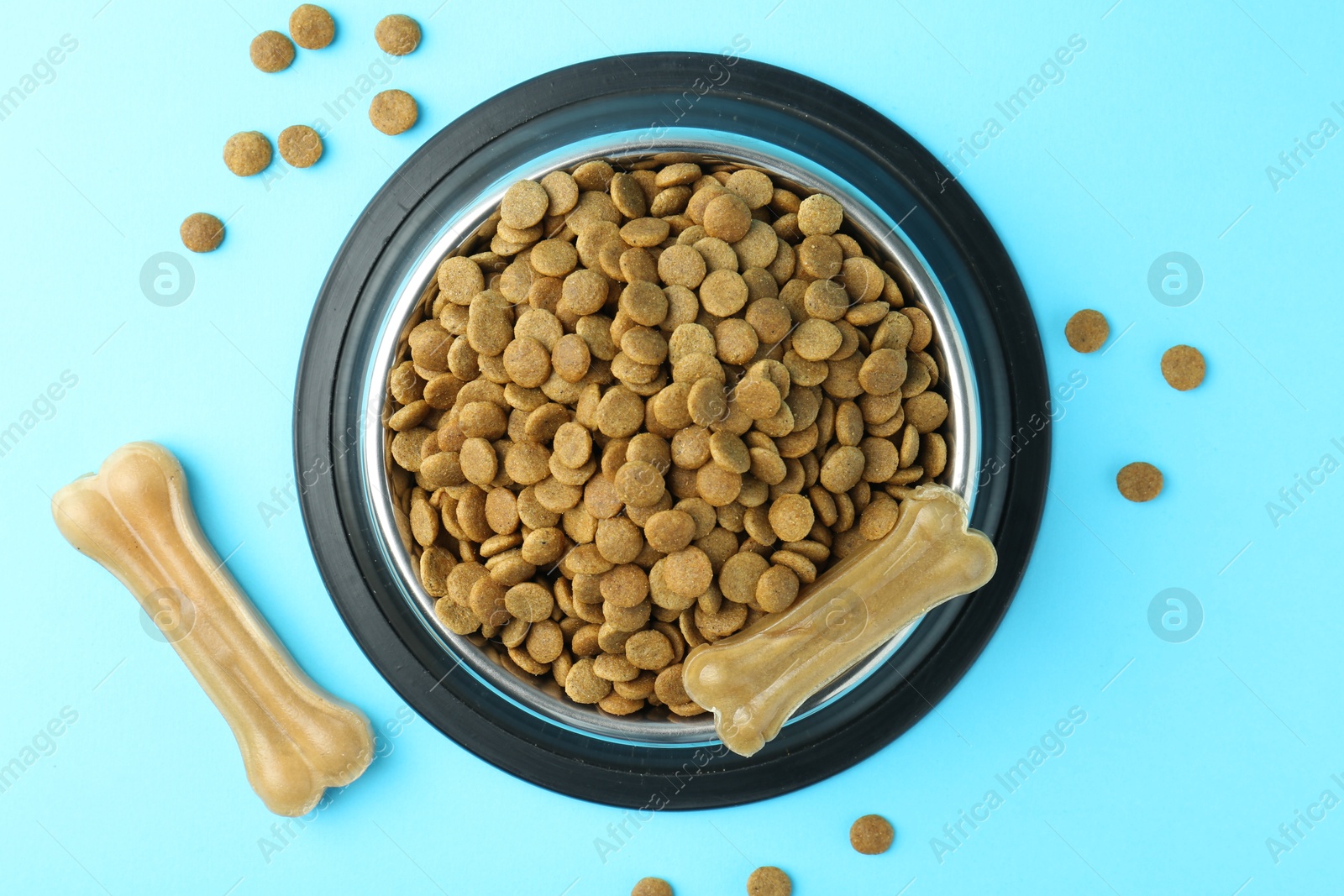 Photo of Dry pet food in feeding bowl and chew bones on light blue background, top view