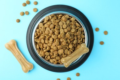 Photo of Dry pet food in feeding bowl and chew bones on light blue background, top view