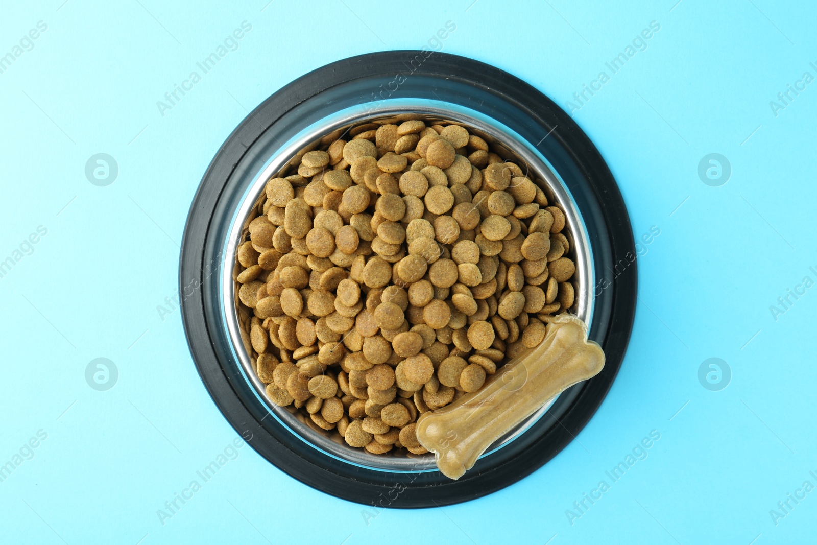 Photo of Dry pet food in feeding bowl and chew bone on light blue background, top view