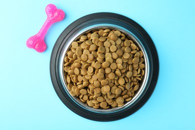 Photo of Dry pet food in feeding bowl and chew bone on light blue background, flat lay