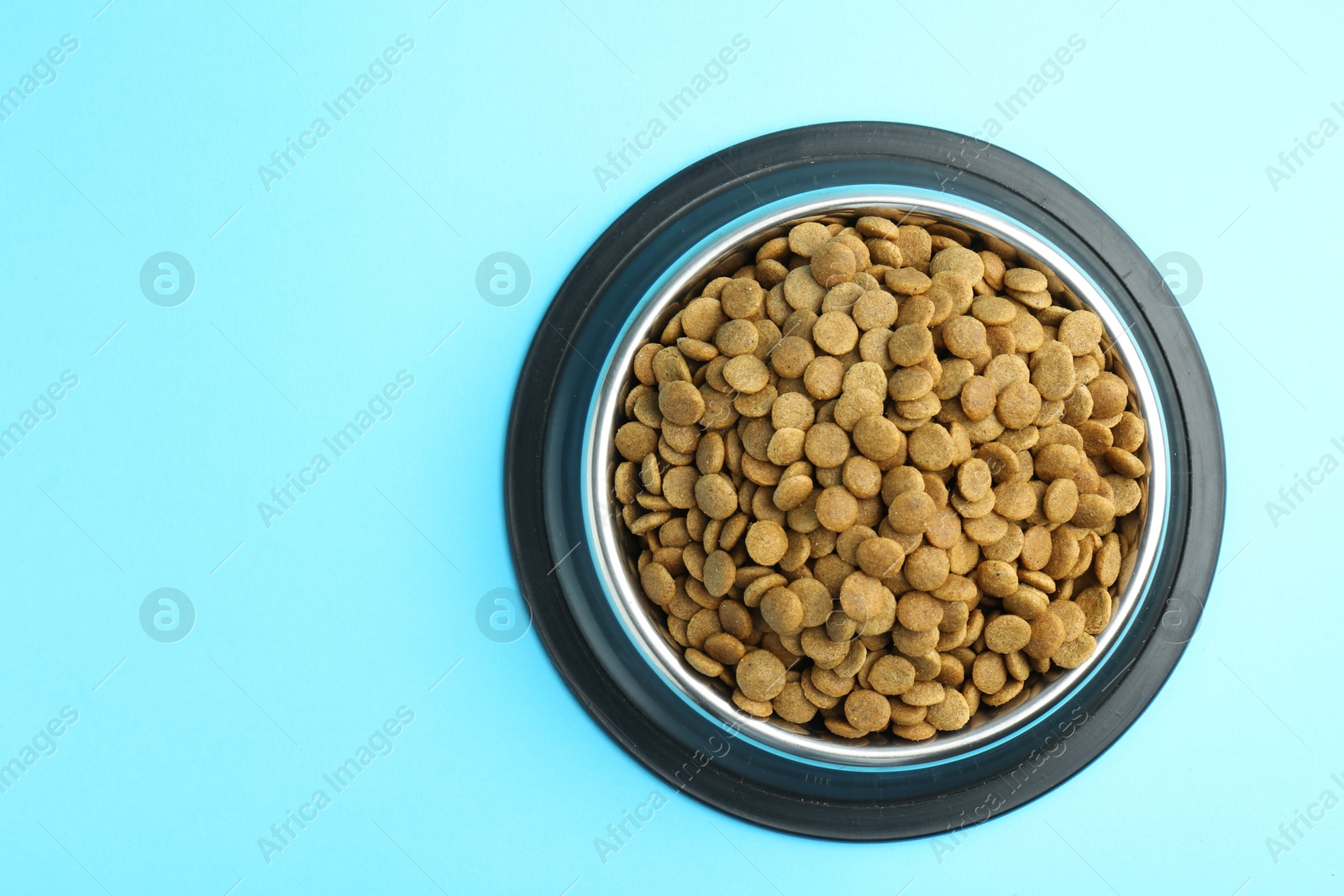 Photo of Dry pet food in feeding bowl on light blue background, top view. Space for text