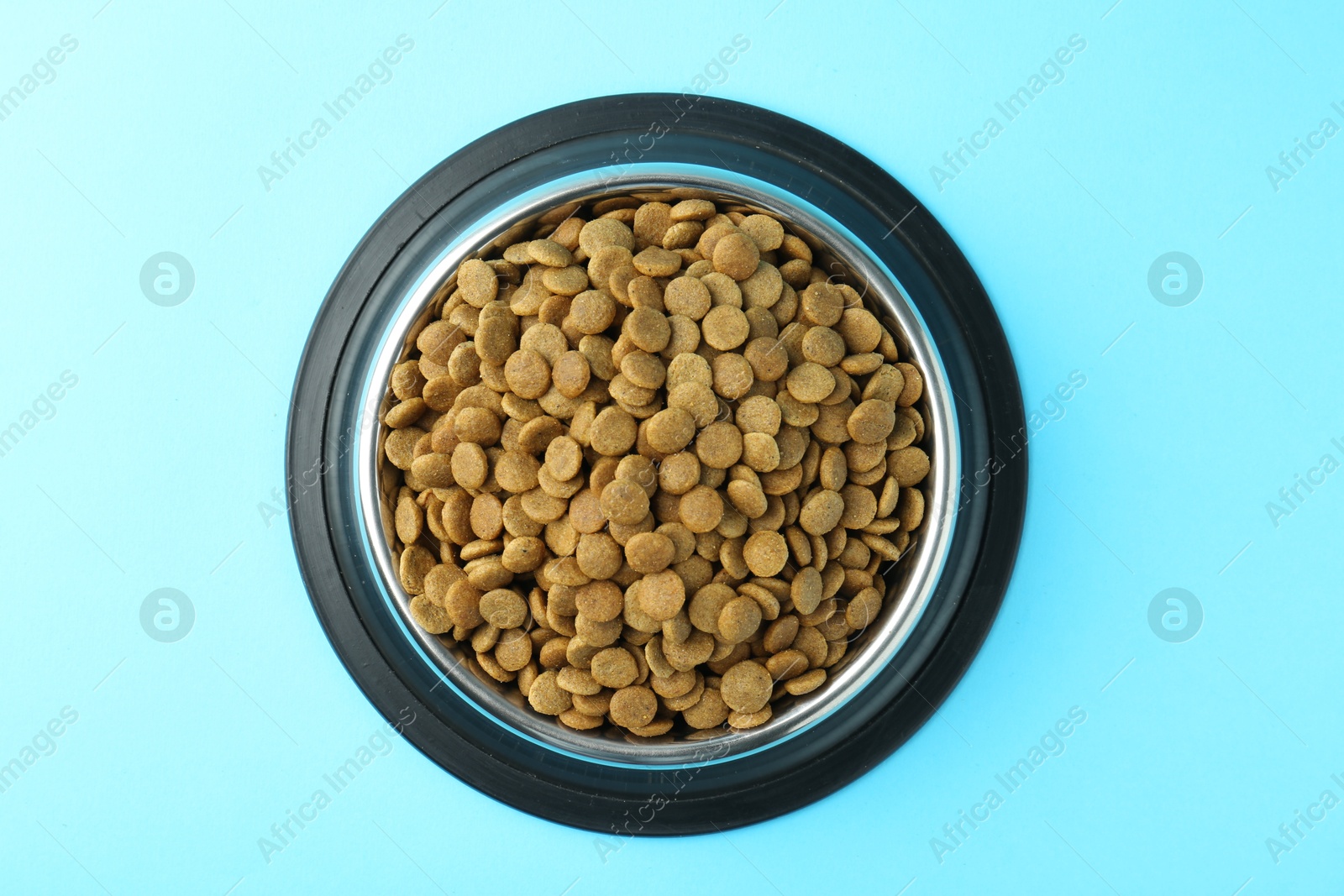 Photo of Dry pet food in feeding bowl on light blue background, top view