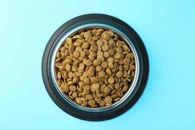 Photo of Dry pet food in feeding bowl on light blue background, top view