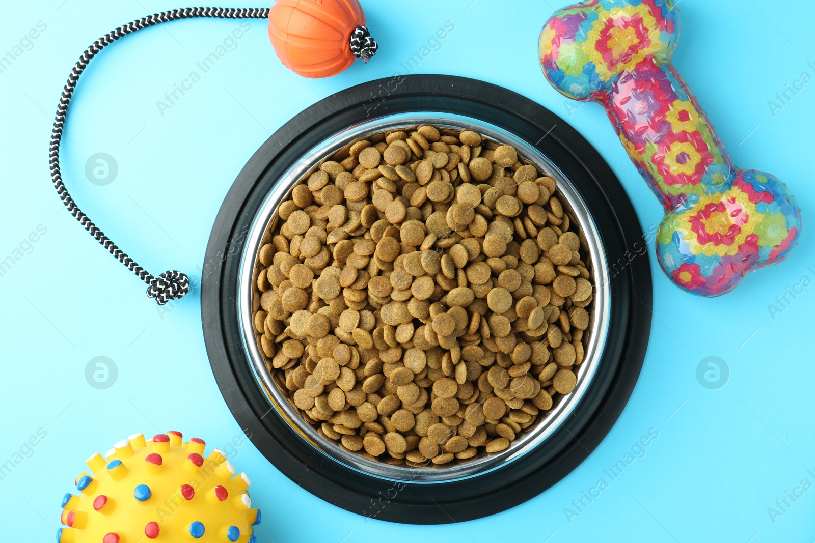 Photo of Dry pet food in feeding bowl and toys on light blue background, flat lay