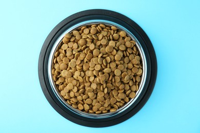 Photo of Dry pet food in feeding bowl on light blue background, top view