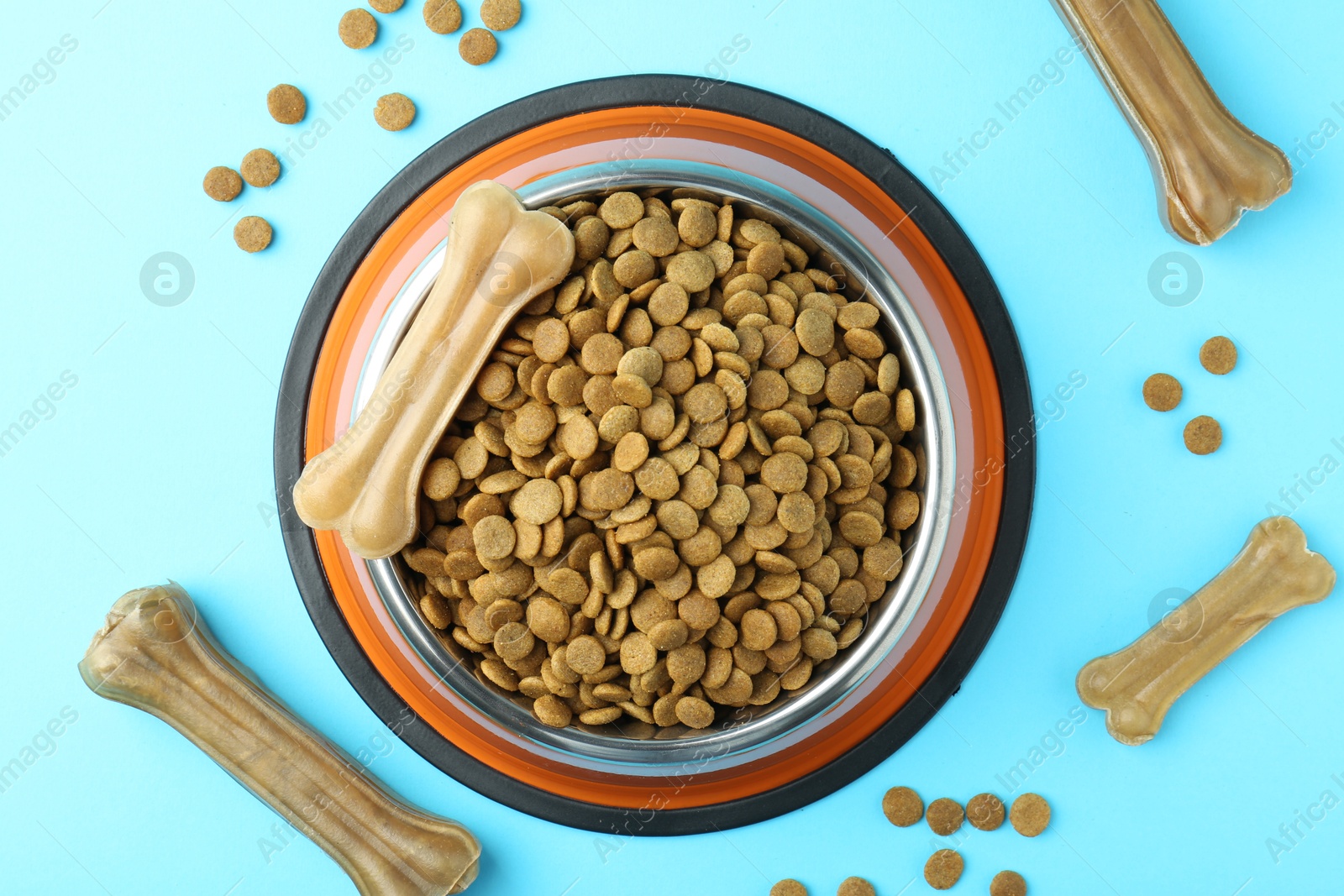 Photo of Dry pet food in feeding bowl and chew bones on light blue background, top view