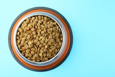 Photo of Dry pet food in feeding bowl on light blue background, top view. Space for text