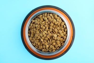 Photo of Dry pet food in feeding bowl on light blue background, top view