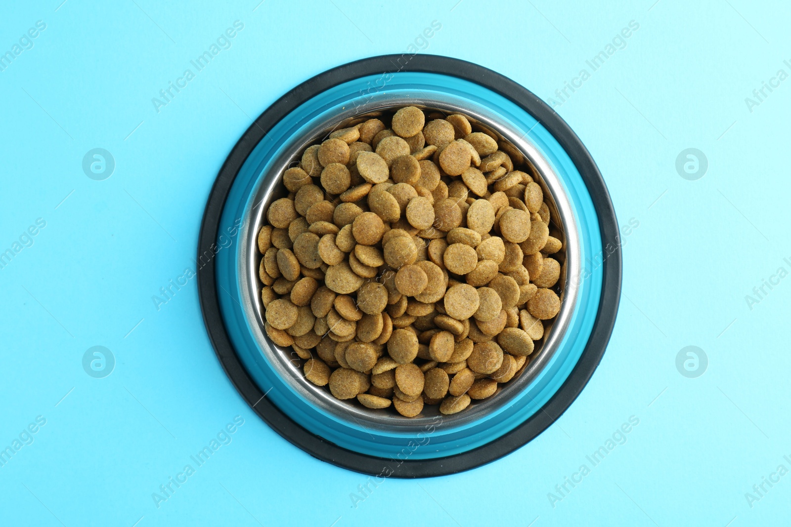 Photo of Dry pet food in feeding bowl on light blue background, top view