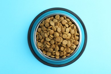 Photo of Dry pet food in feeding bowl on light blue background, top view