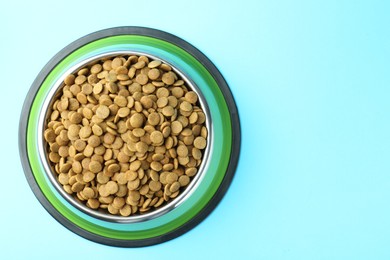 Photo of Dry pet food in feeding bowl on light blue background, top view. Space for text