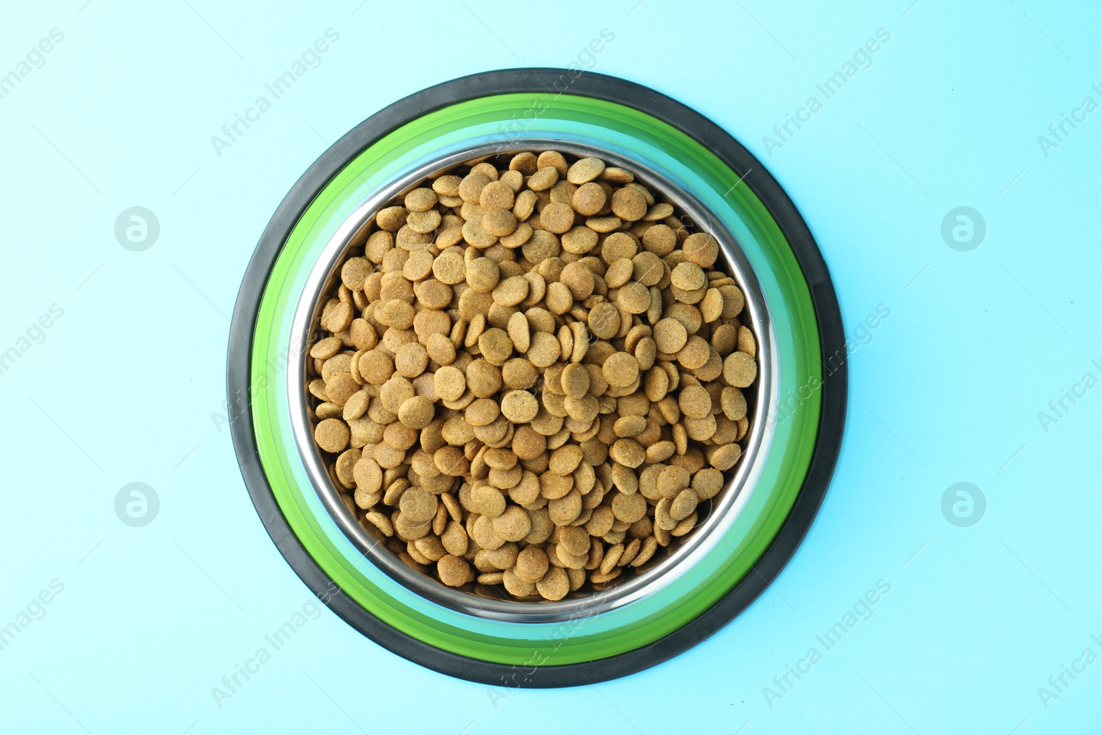 Photo of Dry pet food in feeding bowl on light blue background, top view