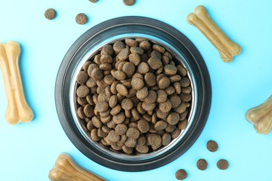 Photo of Dry pet food in feeding bowl and chew bones on light blue background, top view