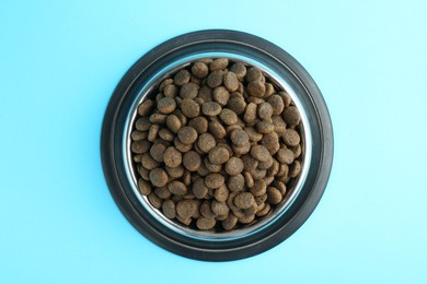 Photo of Dry pet food in feeding bowl on light blue background, top view