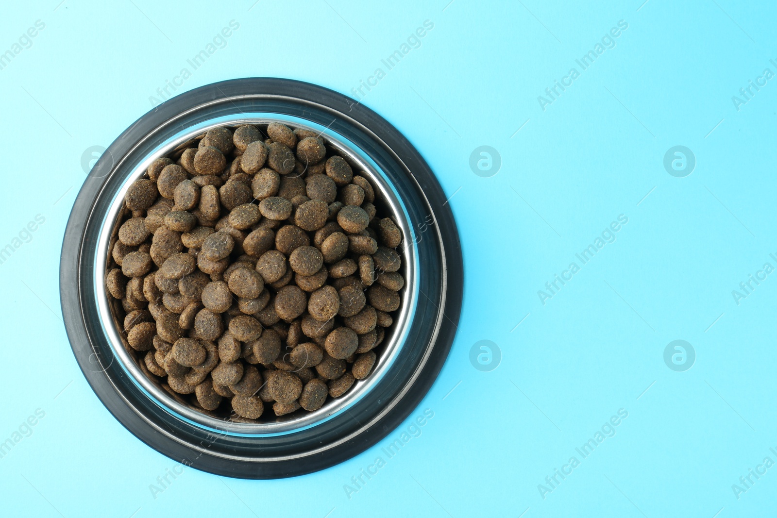 Photo of Dry pet food in feeding bowl on light blue background, top view. Space for text