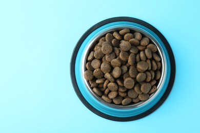 Photo of Dry pet food in feeding bowl on light blue background, top view. Space for text