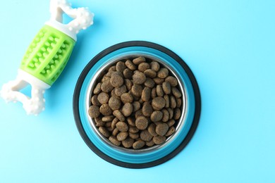 Photo of Dry pet food in feeding bowl and chew bone on light blue background, flat lay