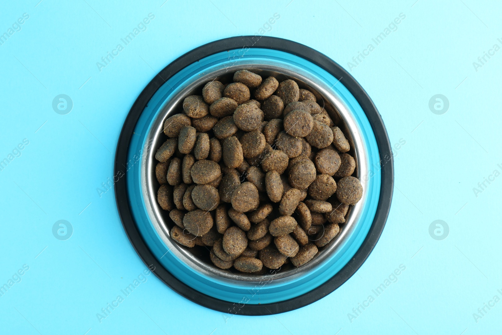 Photo of Dry pet food in feeding bowl on light blue background, top view