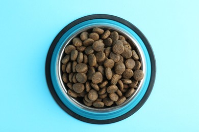 Photo of Dry pet food in feeding bowl on light blue background, top view