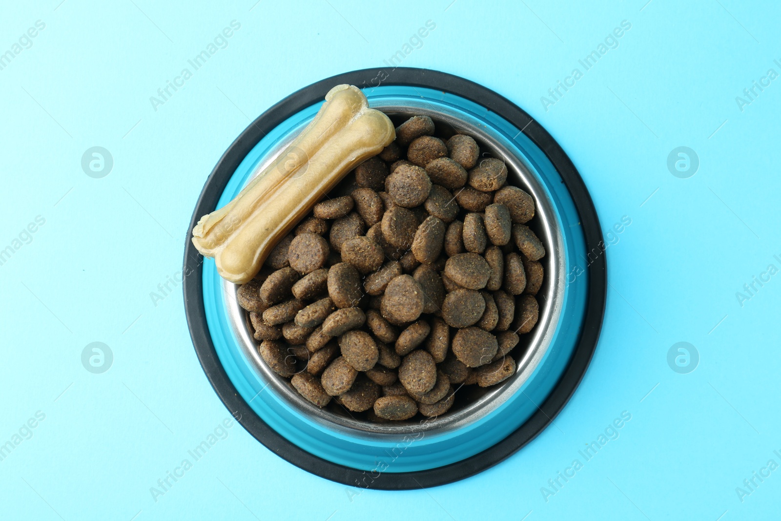 Photo of Dry pet food in feeding bowl and chew bone on light blue background, top view