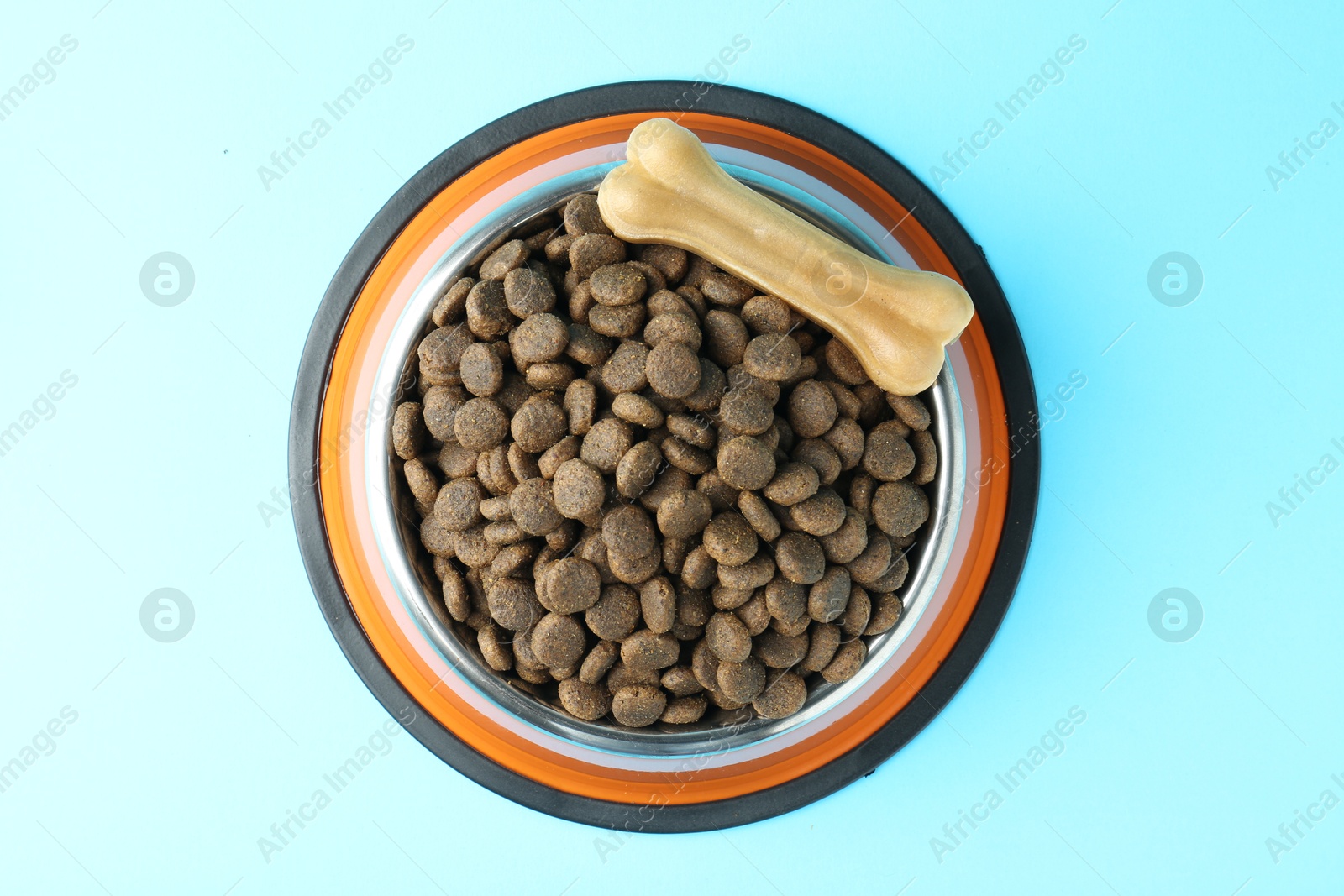 Photo of Dry pet food in feeding bowl and chew bone on light blue background, top view