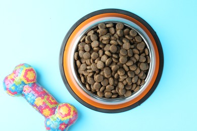 Photo of Dry pet food in feeding bowl and chew bone on light blue background, flat lay