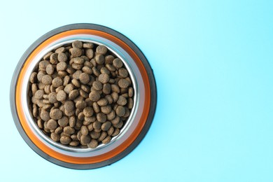 Photo of Dry pet food in feeding bowl on light blue background, top view. Space for text