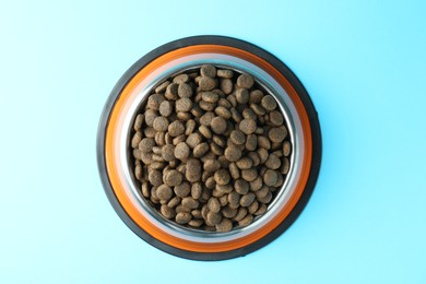 Photo of Dry pet food in feeding bowl on light blue background, top view