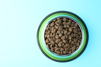 Photo of Dry pet food in feeding bowl on light blue background, top view. Space for text