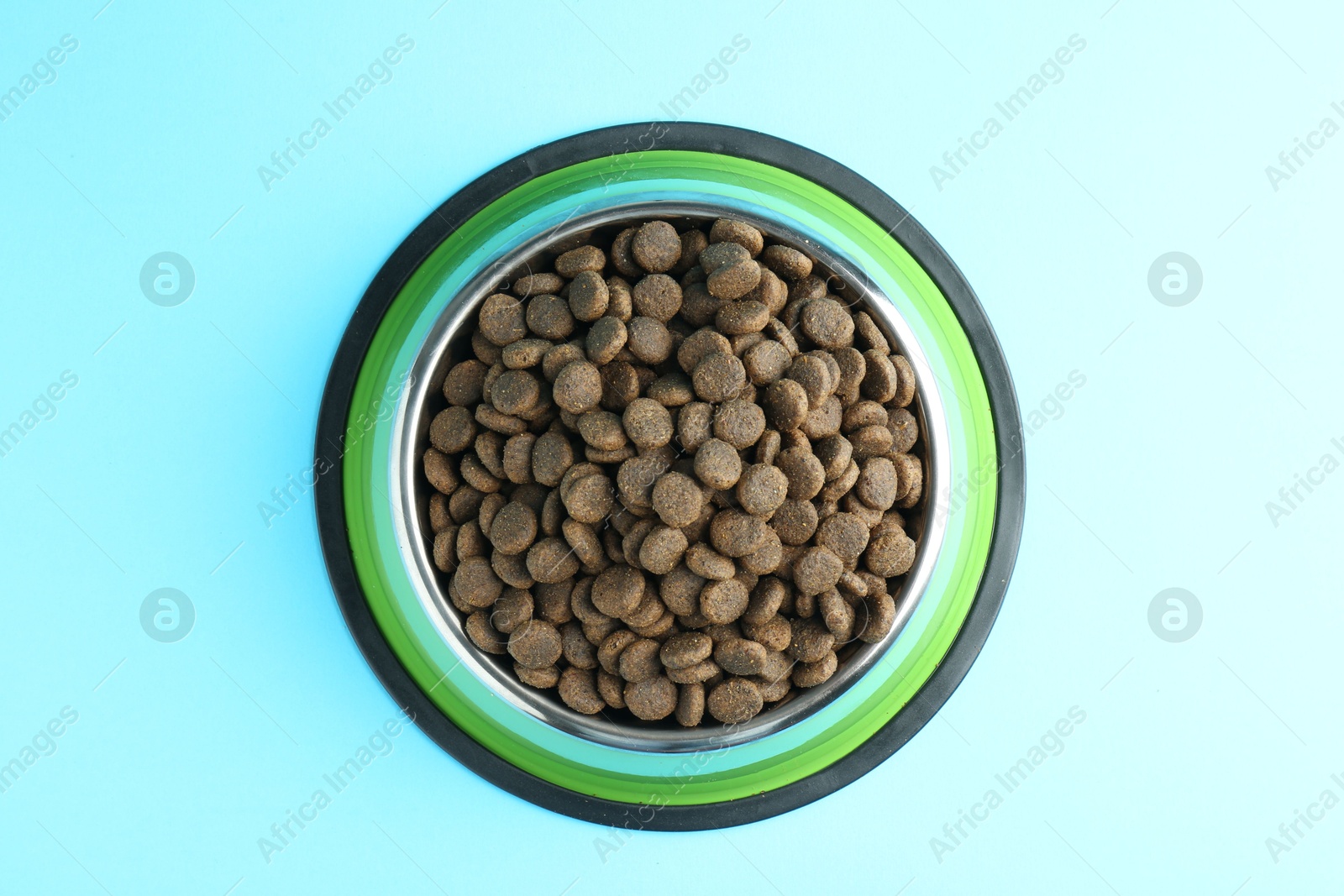 Photo of Dry pet food in feeding bowl on light blue background, top view