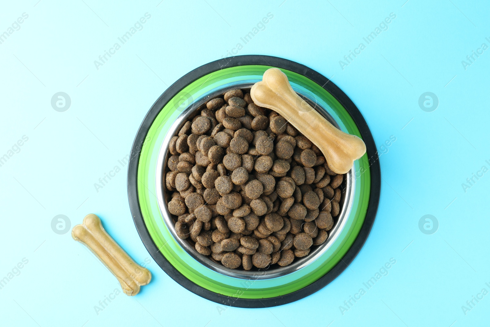 Photo of Dry pet food in feeding bowl and chew bones on light blue background, top view