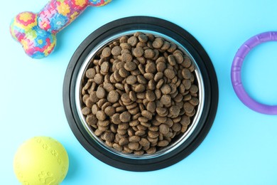 Photo of Dry pet food in feeding bowl and toys on light blue background, flat lay