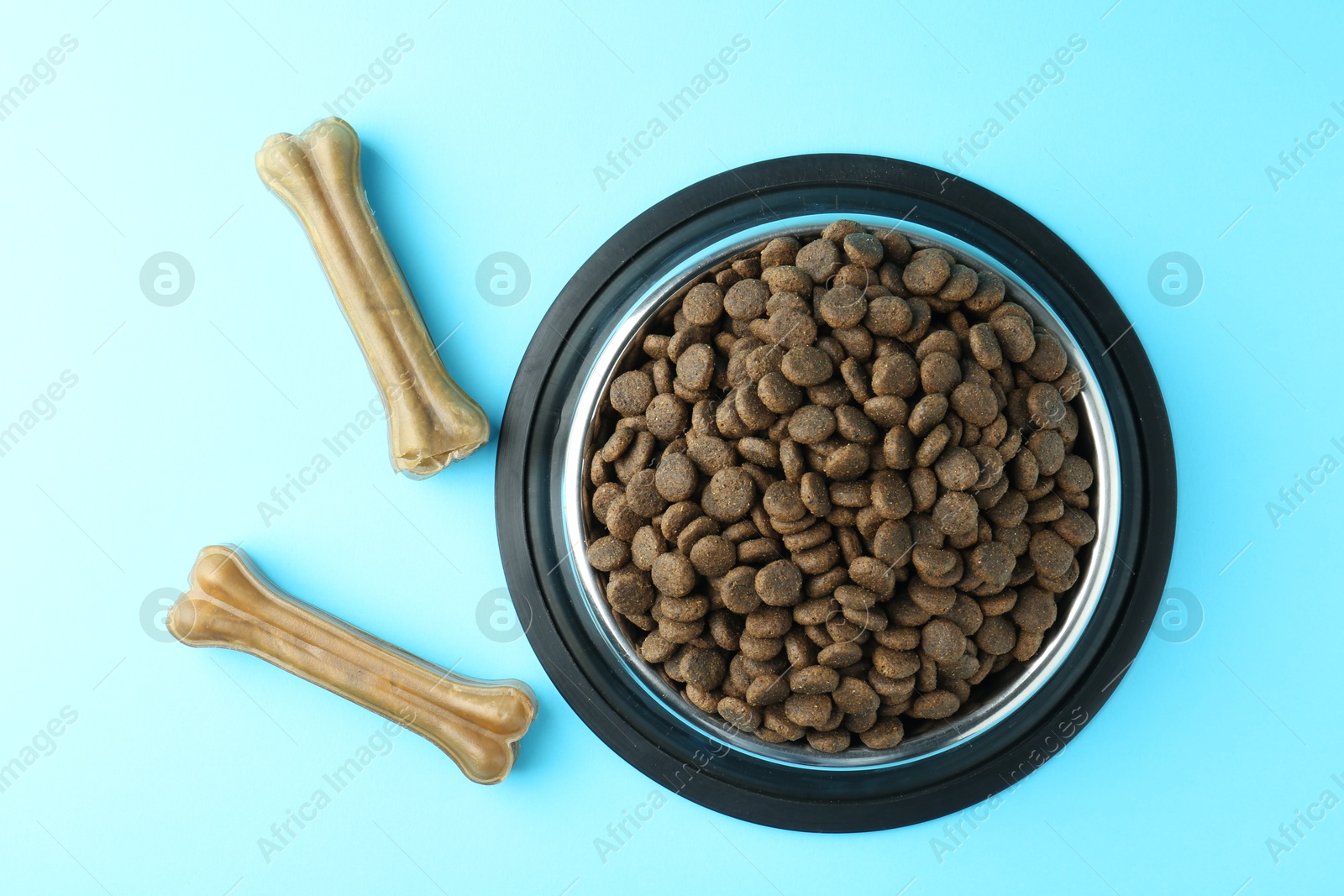 Photo of Dry pet food in feeding bowl and chew bones on light blue background, top view