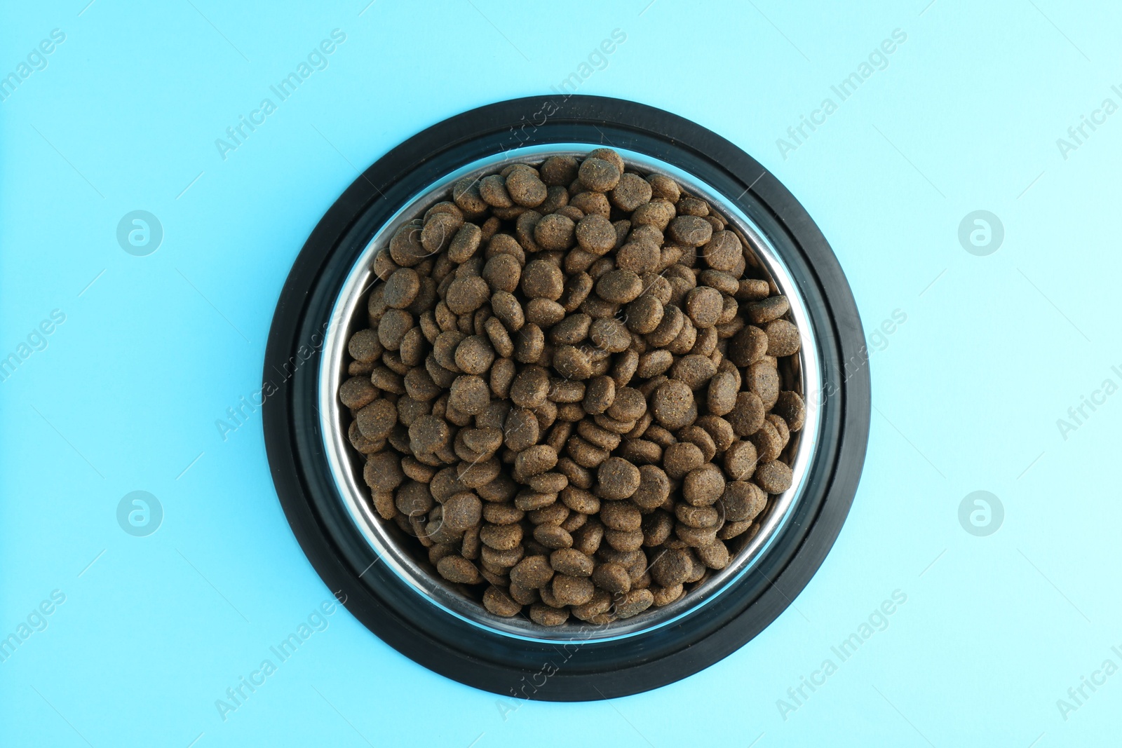 Photo of Dry pet food in feeding bowl on light blue background, top view