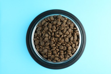 Photo of Dry pet food in feeding bowl on light blue background, top view