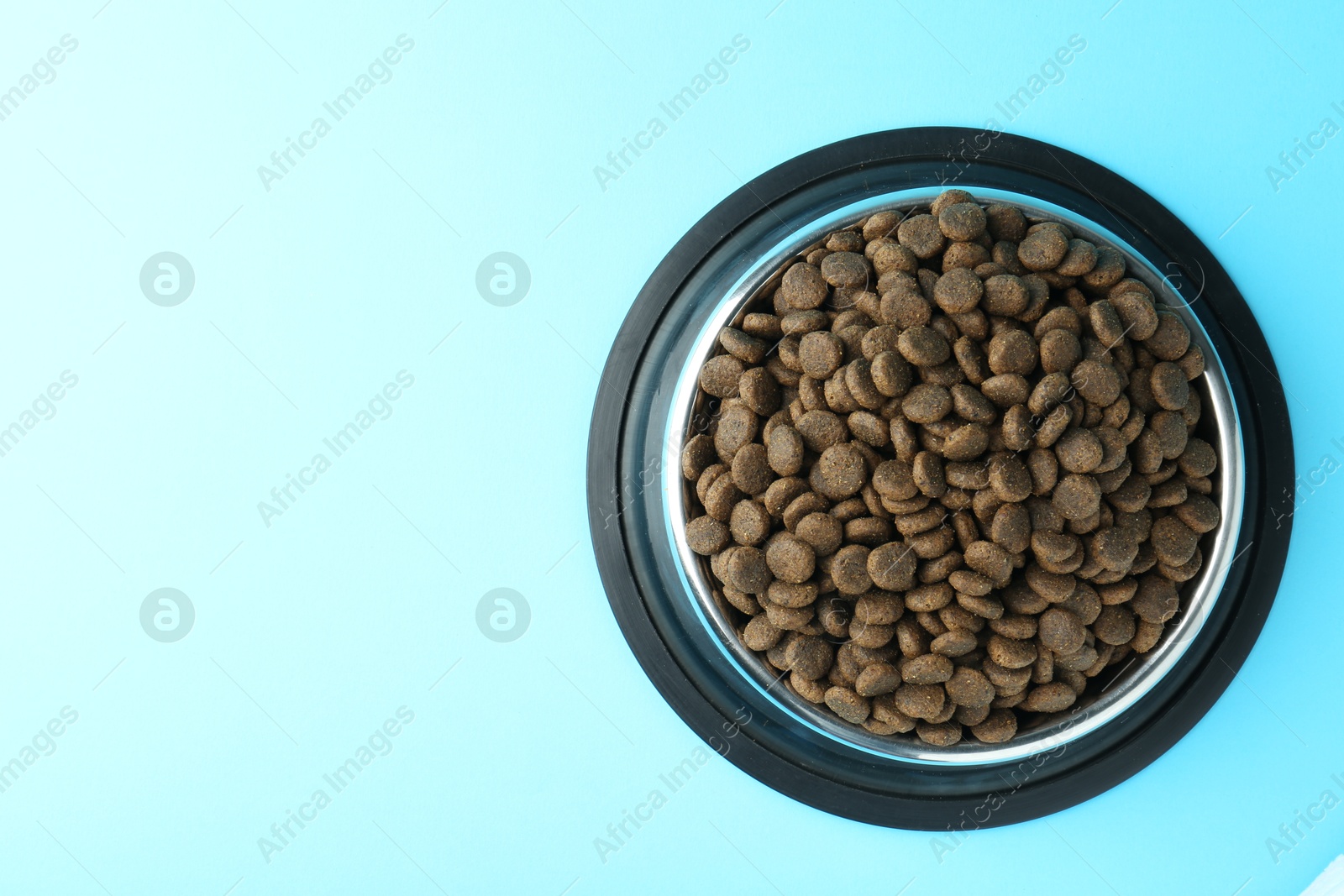 Photo of Dry pet food in feeding bowl on light blue background, top view. Space for text